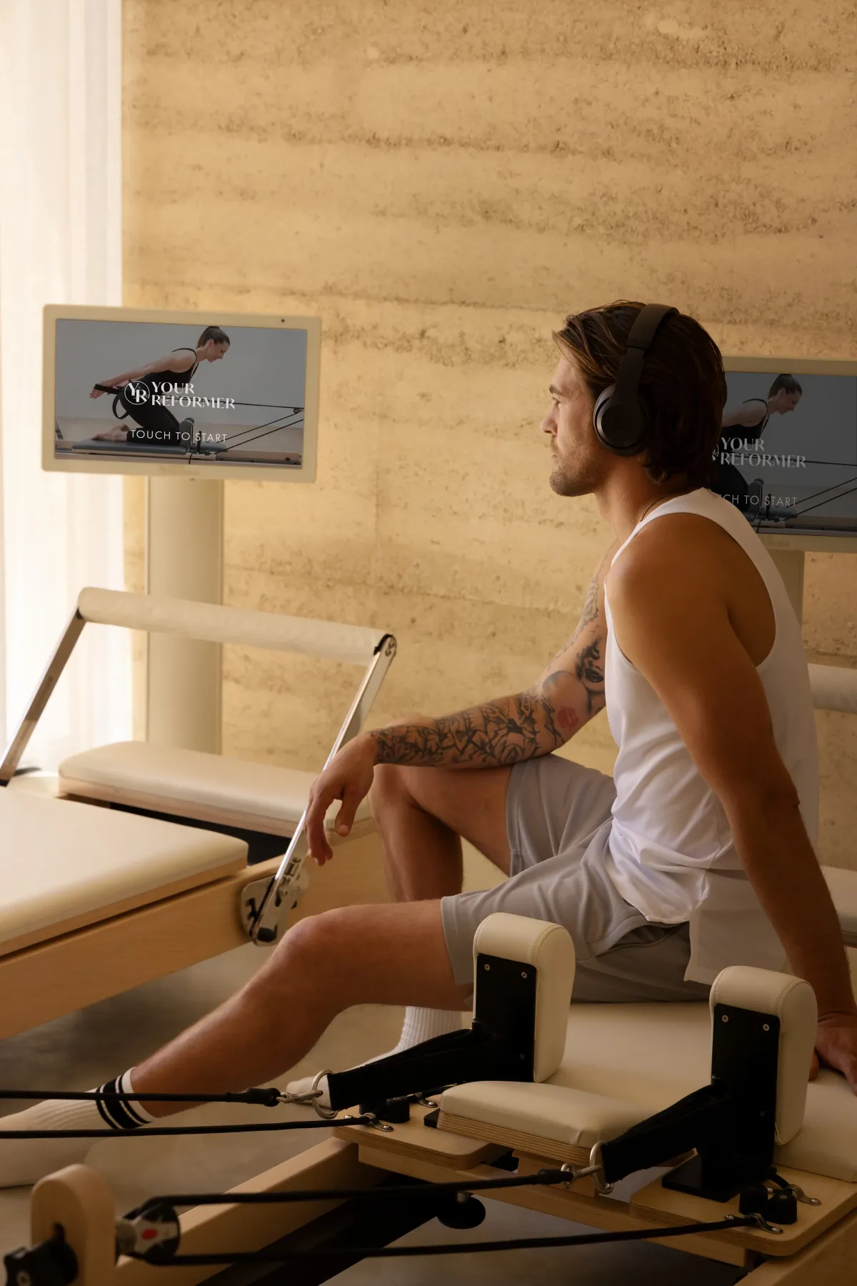 Guest in headphones seated on a reformer, watching a video guided session on the kiosk screen
