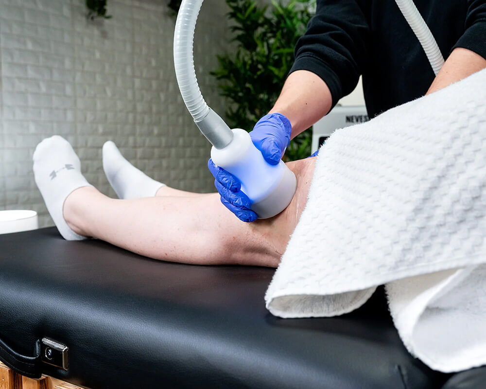 Gloved practitioner smoothing the CryoSkin wand along a client's leg during a toning session