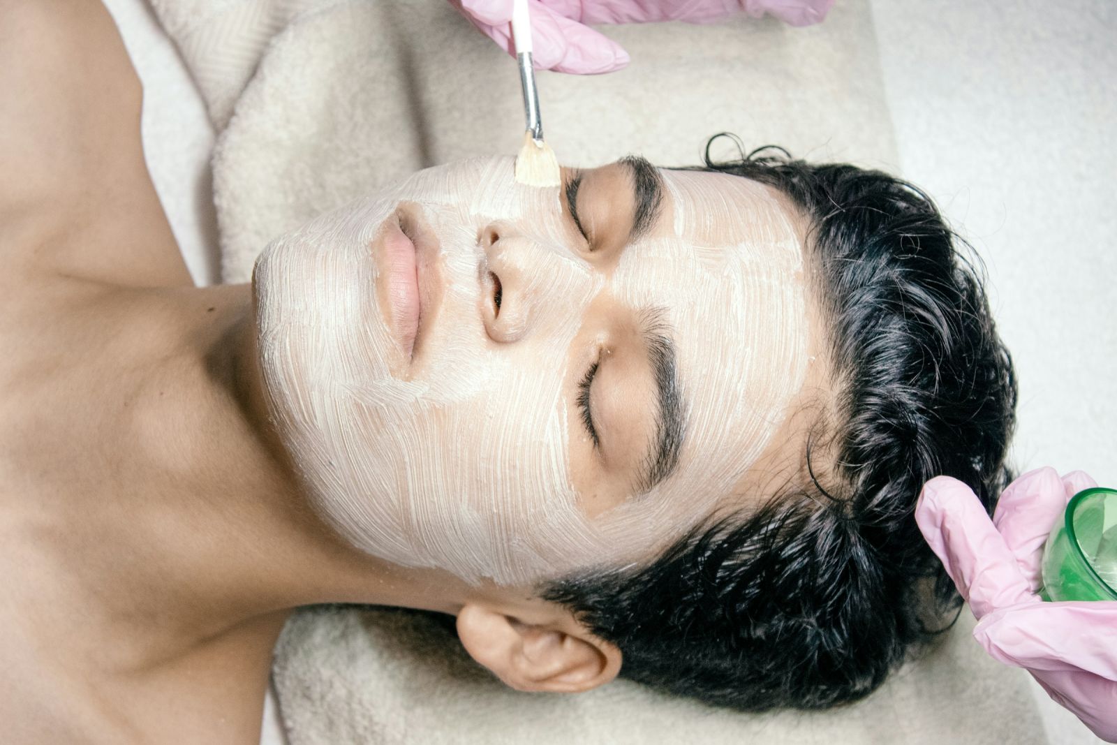Esthetician brushing a creamy mask onto a client's face