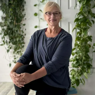 Mandi Edwards seated in the studio with trailing green plants behind