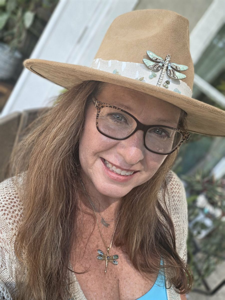 Robin Leathers smiling in a wide brimmed hat pinned with a dragonfly brooch